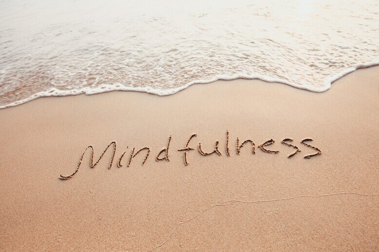 Palavra Mindfulness escrita na area com a água do mar calma