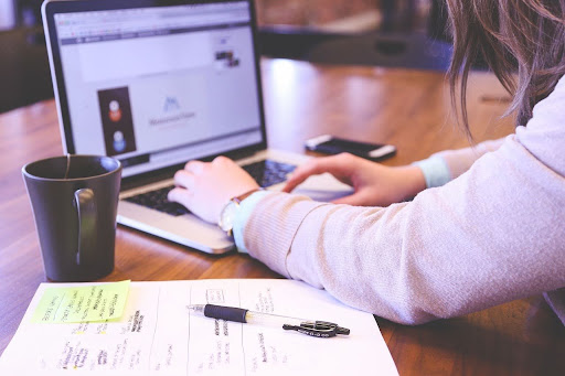 Pessoa digitando em notebook, com xícara de café e anotações em post-its sobre a mesa