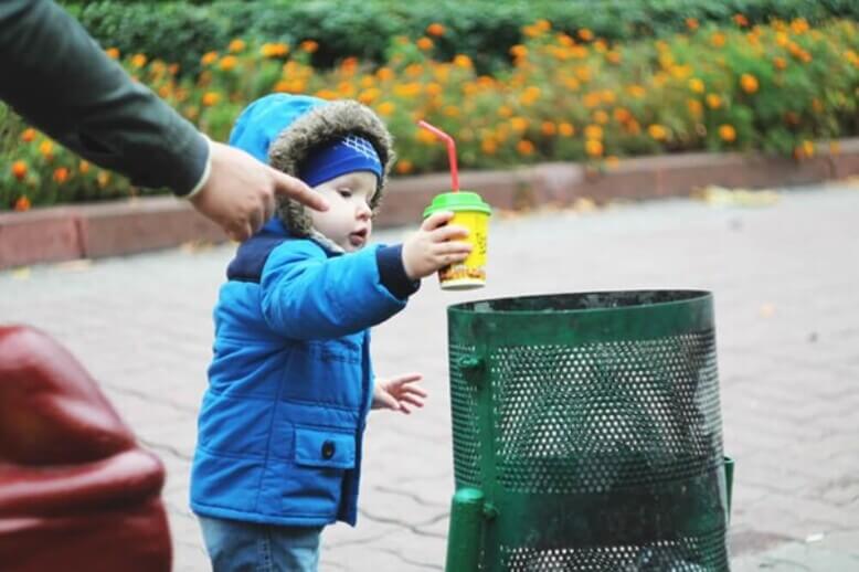 Criança jogando lixo no lugar correto, resultado de boa educação ambiental
