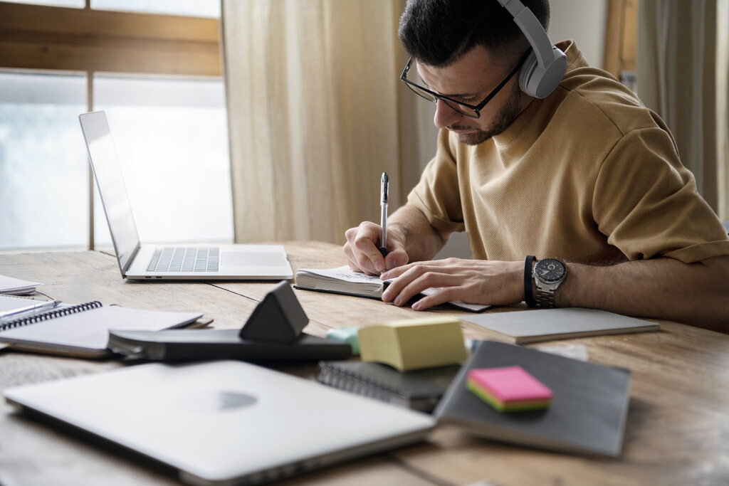 Estudante faz anotações ao lado do notebook, reforçando a importância de manter uma rotina de estudos consistente.