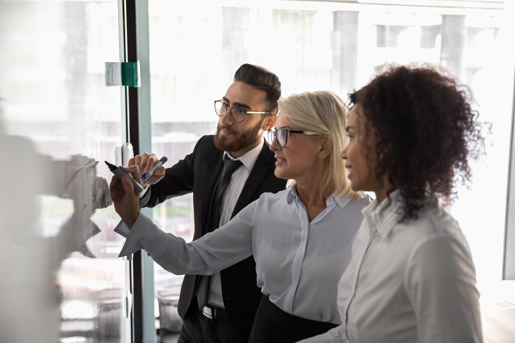 Equipe reunida em frente a quadro de planejamento alinhando estratégias de comunicação interna corporativa.