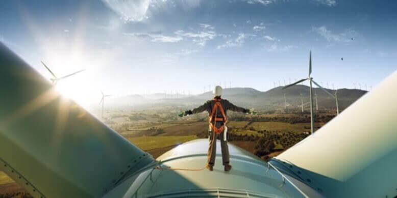 Um homem em cima de um aerogerador em funcionamento para gerar energia limpa