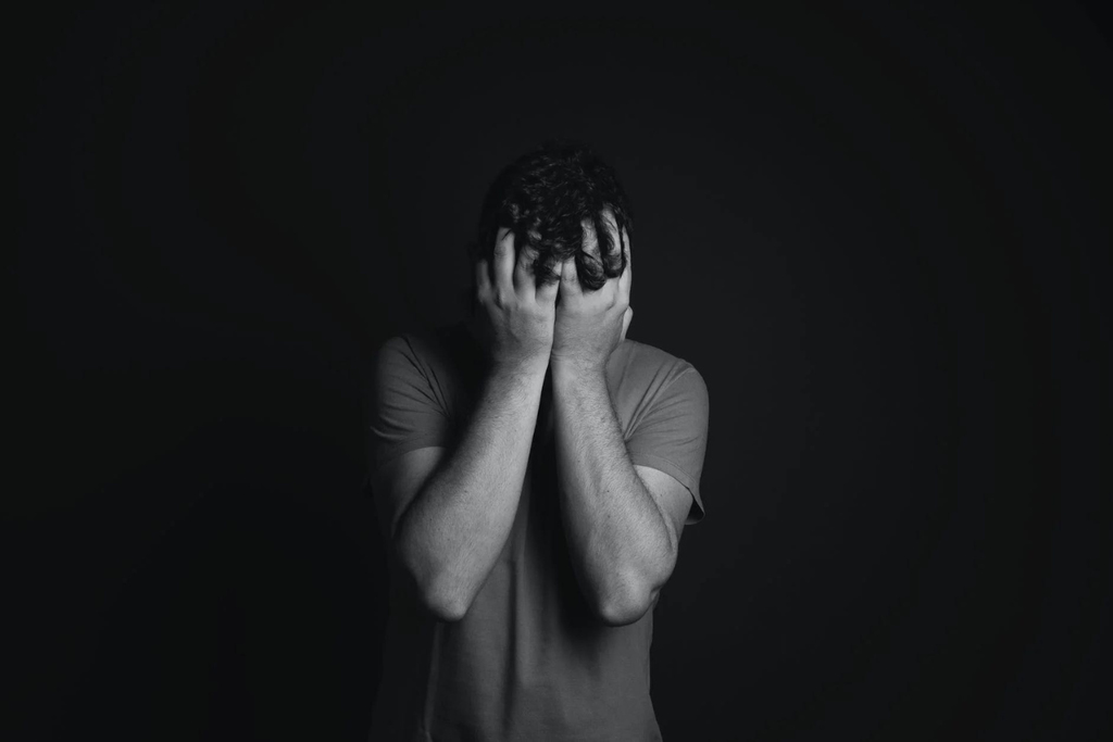Homem em depressão em pé com a cabeça abaixada e mãos no rosto