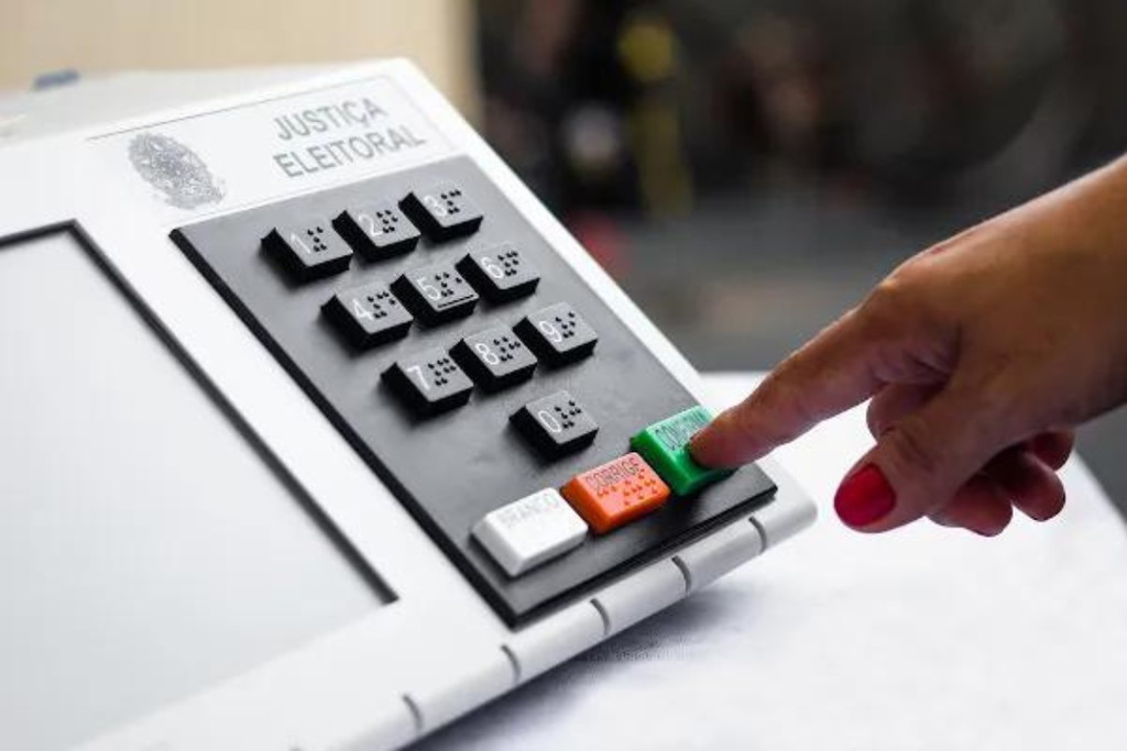Urna eletrônica da justiça eleitoral e uma pessoa confirmando o voto para auditoria