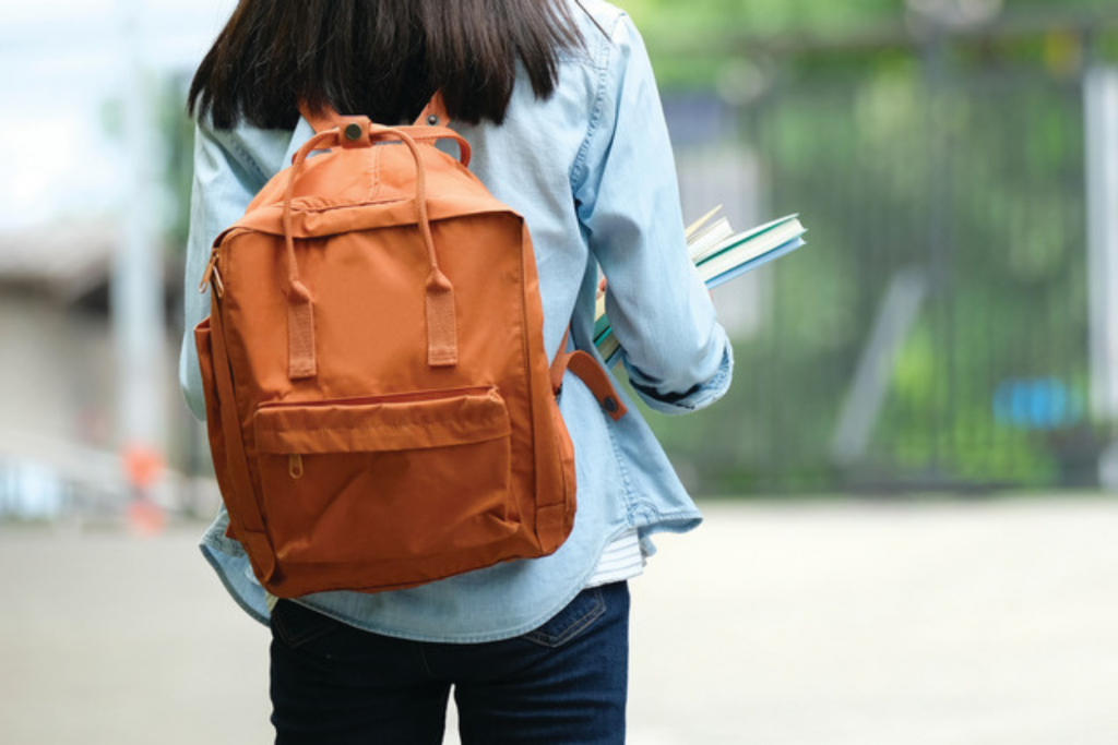 Uma mulher andando com mochila e livros nos braços, evidenciando caracteristicas do modelo de ensino presencial