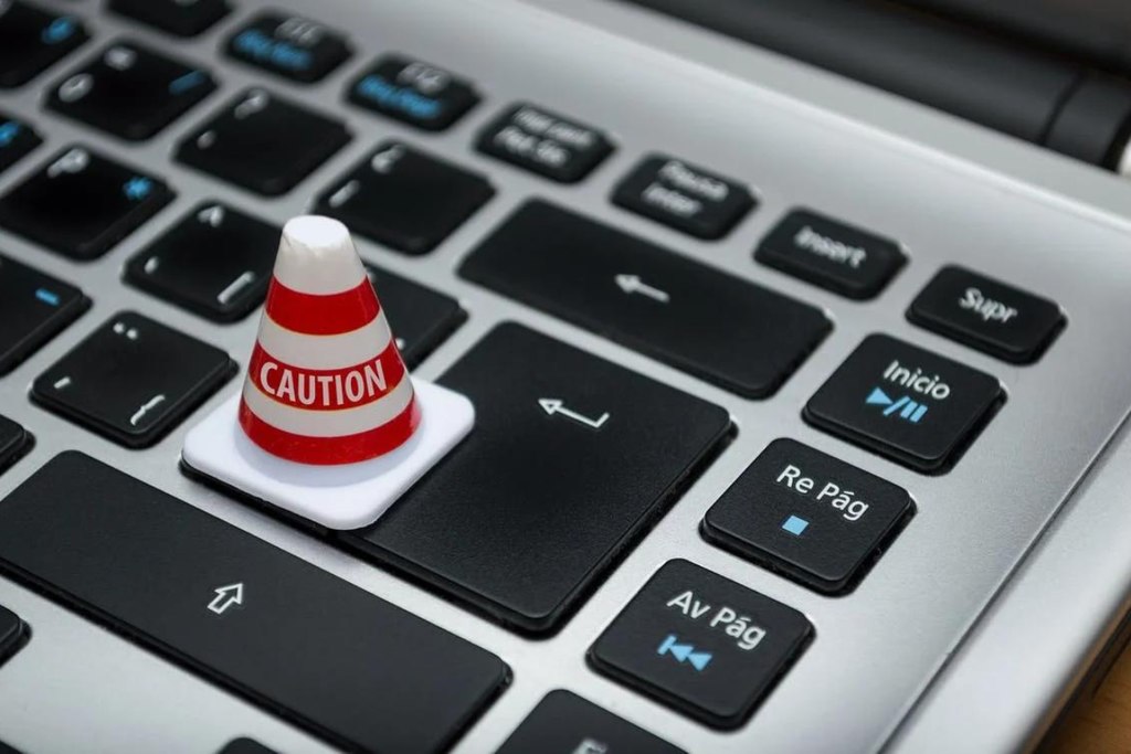 Um cone escrito "cuidado" em inglês em cima do teclado, alertando sobre os cuidados com o vazamento de dados