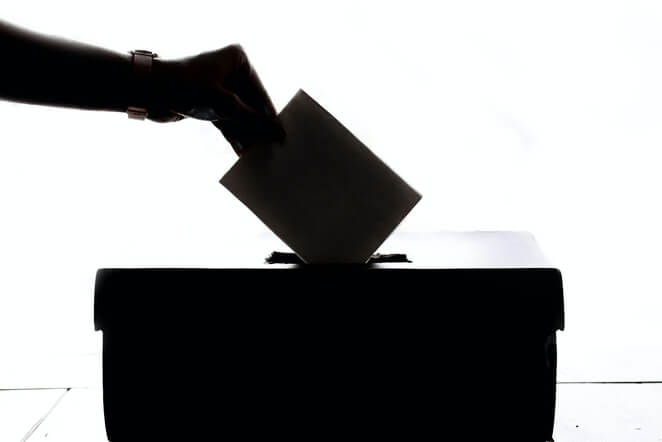 Uma pessoa colocando um envelope em uma caixa simbolizando a eleição em sistemas de governo