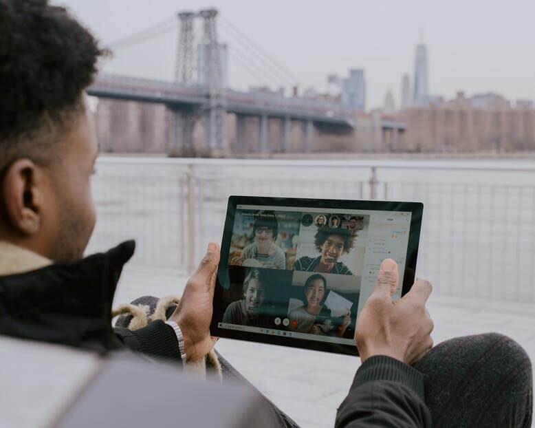 Homem acompanhando reunião pelo tablet em ambiente externo, um dos impactos da pandemia na educação