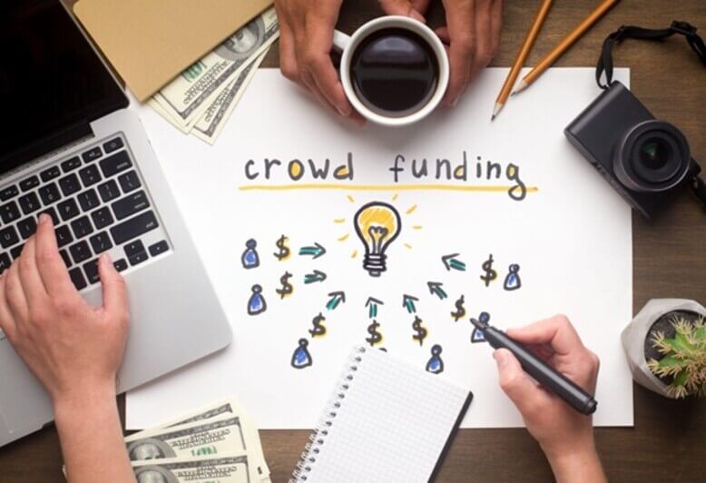 Duas pessoas em uma mesa com a palavra "crowdfunding" escrita em um papel no centro