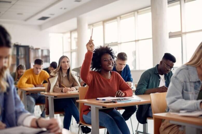 Jovem em sala de aula levantando a mão para dúvida sobre políticas públicas na educação