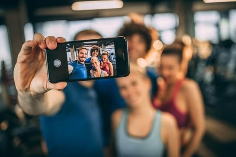 Grupo de amigos utilizando uma das tecnologias espaciais, a camera de smartphone, para tirar uma selfie na academia