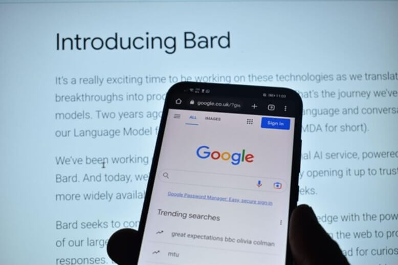 Telefone em frente à uma tela de computador com a introdução ao Bard do Google