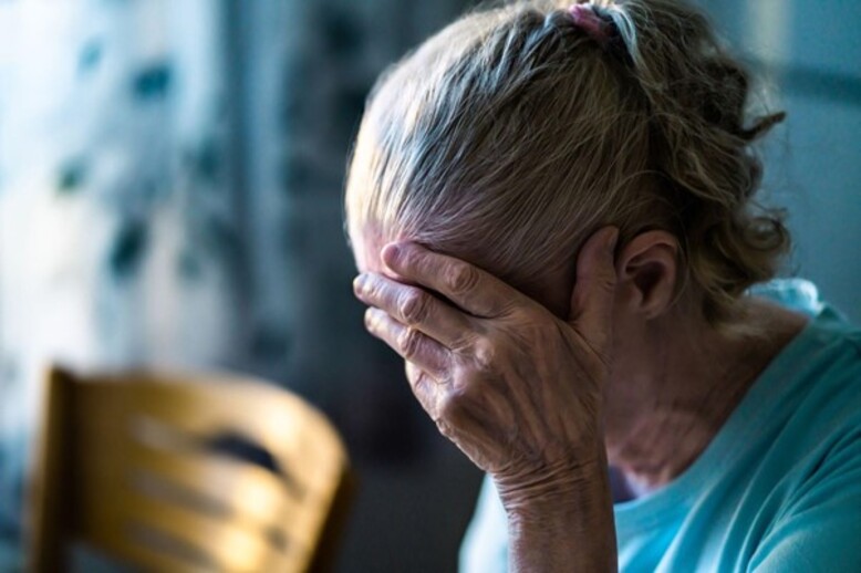 Uma mulher idosa, com o rosto oculto e expressando tristeza, enfrenta a dor da exclusão de oportunidades devido ao etarismo