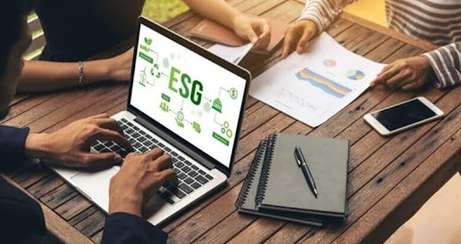 Pessoas reunidas analisando gráficos e notebook com ícones de ESG na tela, analisando estratégias de sustentabilidade empresarial