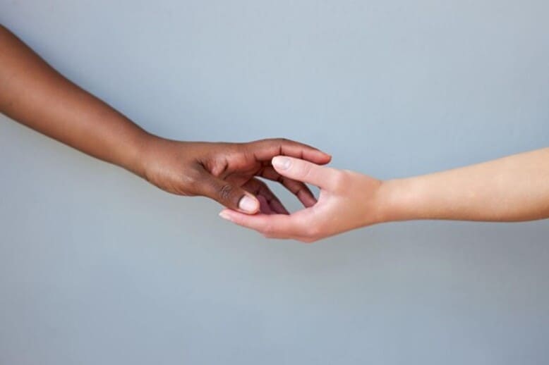Aperto de mãos entre pessoa negra e pessoa branca como simbolo de esperança do fim da desigualdade racial no Brasil