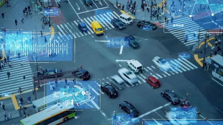 Uma vista de um cruzamento em uma cidade inteligente com diversos carros passando enquanto dados são coletados, representados por elementos holográficos na imagem