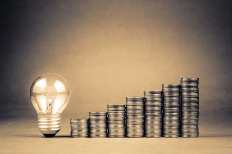 Uma lâmpada acessa em meio a moedas indica o valor da inovação tecnológica no mercado empresarial