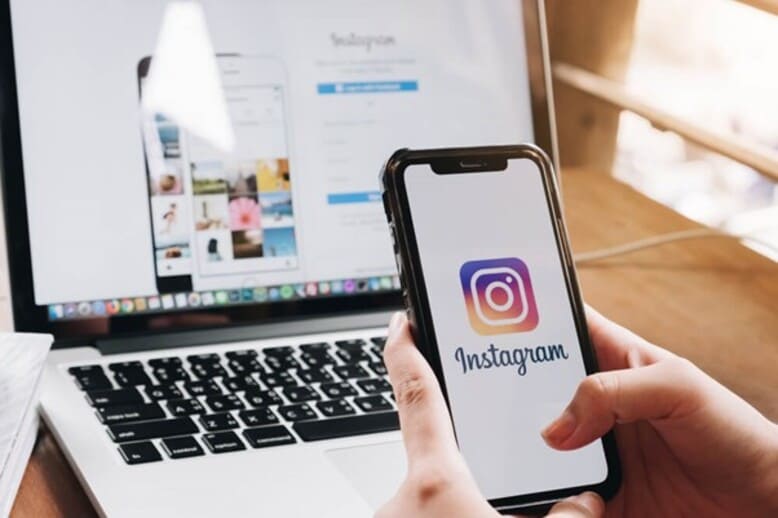 Pessoa acessando a rede social Instagram pelo notebook e smartphone para executar suas estratégias de automação de marketing digital