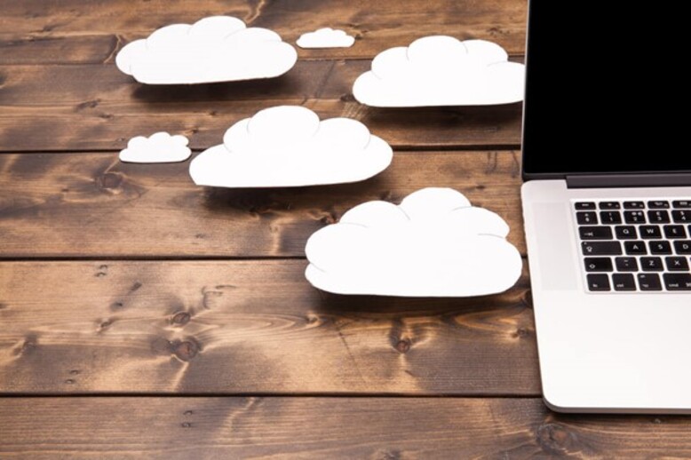 Laptop em cima de uma mesa com nuvens ao lado representando a computação em nuvem
