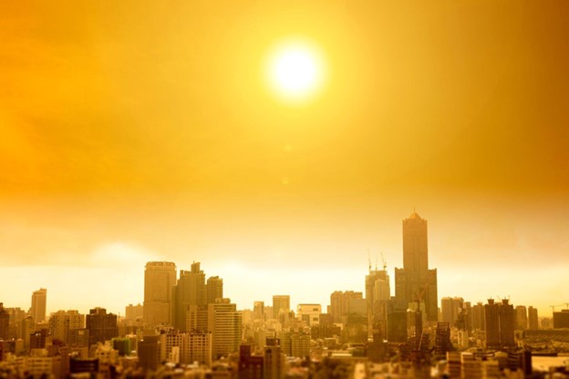 Silhueta da cidade sob um sol escaldante, com o céu tingido em tons de laranja e amarelo, indicando a ebolição global