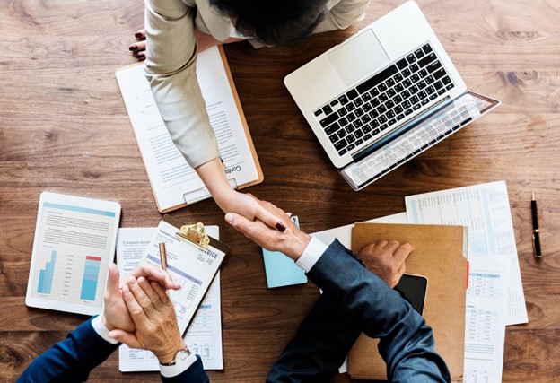 Duas pessoas apertando as mãos em uma reunião de negócios com documentos e laptops na mesa