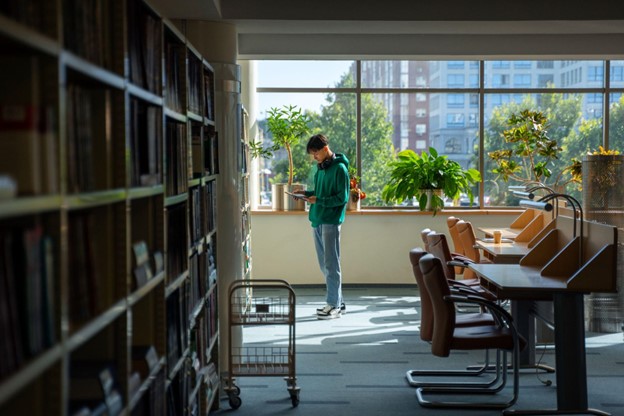 Estudante em biblioteca explorando livros, representando pesquisa sobre grade curricular economia em instituições acadêmicas.