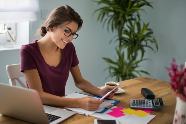 Mulher sorrindo trabalha com econometria em ambiente organizado, utilizando calculadora, laptop e anotações.