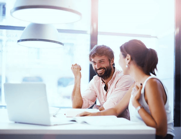 Duas pessoas discutindo sobre Economia Criativa em um ambiente de escritório moderno, com um laptop e documentos sobre a mesa.