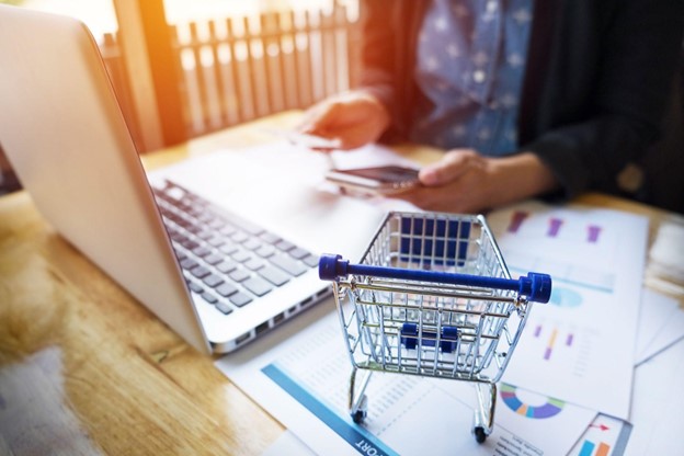 Carrinho de compras em miniatura ao lado de um laptop, simbolizando o empreendedorismo digital.