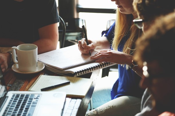 Grupo de profissionais colaborando em estratégias de Value-Based Management, com anotações e laptops em um ambiente de trabalho informal.