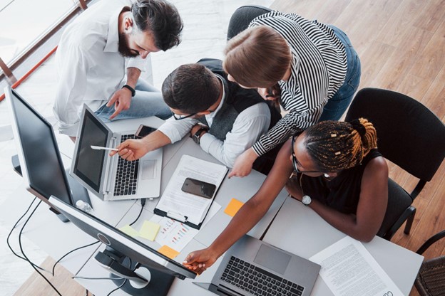 Equipe colaborativa analisa projeto em ambiente tecnológico, destacando a flexibilidade no trabalho e inovação.