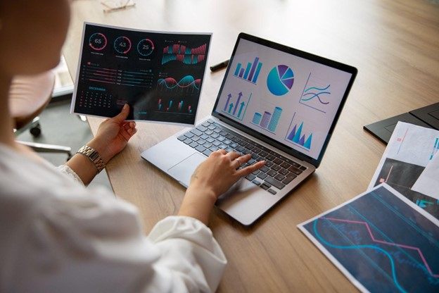 Profissional analisando gráficos no laptop e em papel, aplicando métodos quantitativos para tomada de decisão estratégica.