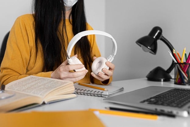 Mulher com fones de ouvido e máscara estuda em ambiente acadêmico, explorando o que é doutorado profissional e seus benefícios.