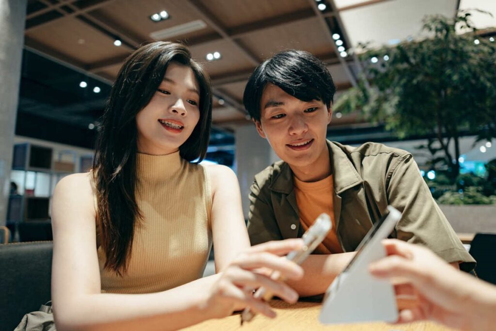 Dois jovens em um ambiente moderno olhando para um celular, representando interação digital e pagamento compartilhado.