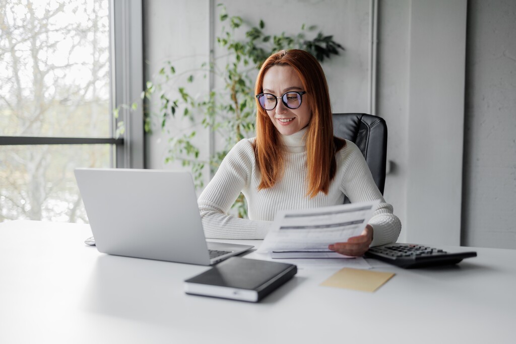 Mulher analisando documentos e calculando informações no escritório para elaborar carta de motivação.