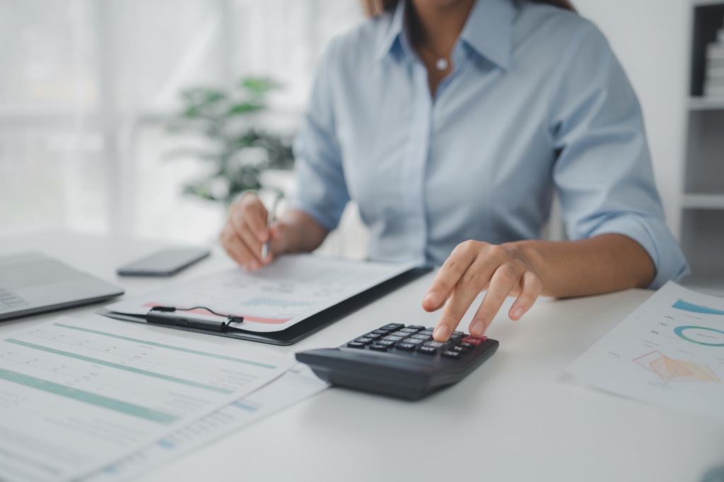Profissional utiliza calculadora e documentos para elaborar projeções e controlar despesas da empresa.