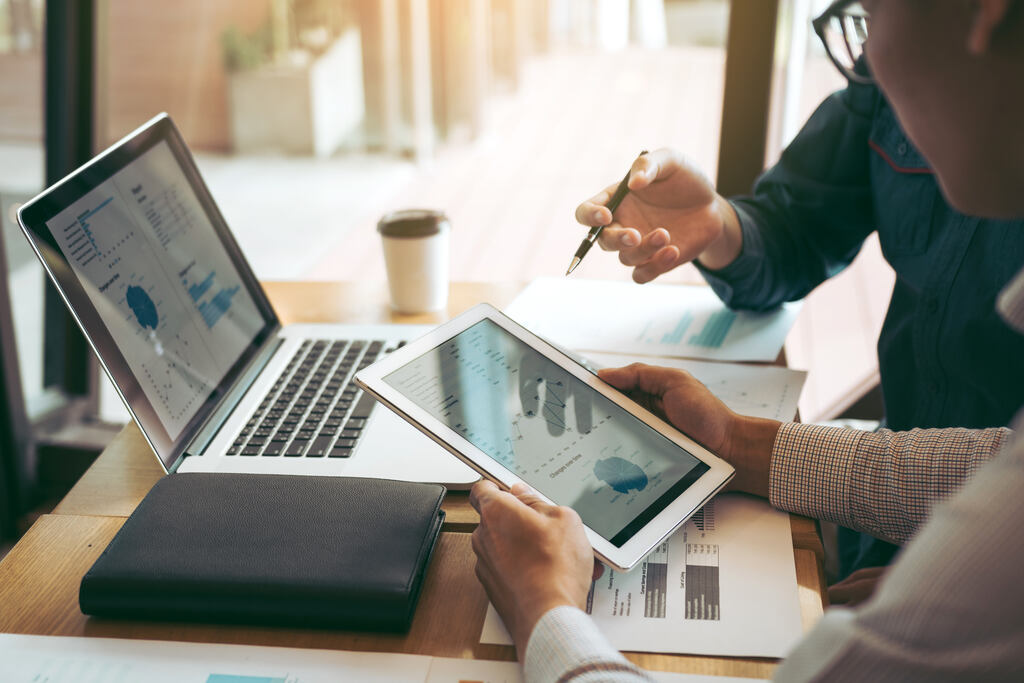Profissionais analisam gráficos em tablet e notebook durante o planejamento orçamentário empresarial.