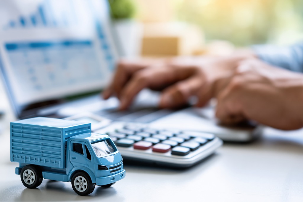 Miniatura de caminhão, calculadora e notebook ilustram o cálculo da balança comercial e do saldo entre países.