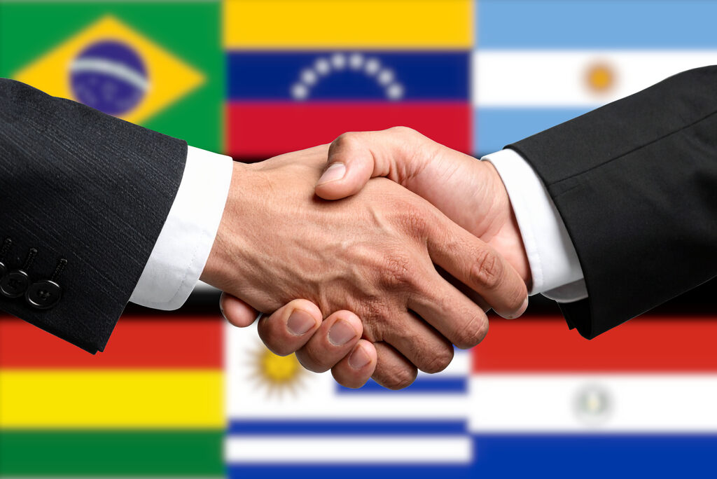 Aperto de mãos entre representantes de países simboliza cooperação internacional e acordos multilaterais.